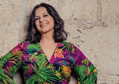 Olga Cerpa sonriente junto a un muro de piedra, con una blusa de flores de colores.