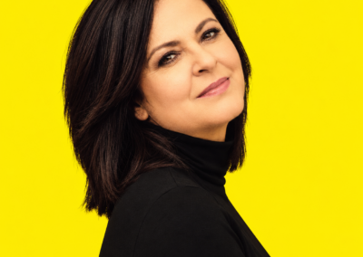 Retrato de Olga Cerpa con jersey negro de cuello alto sobre fondo amarillo.